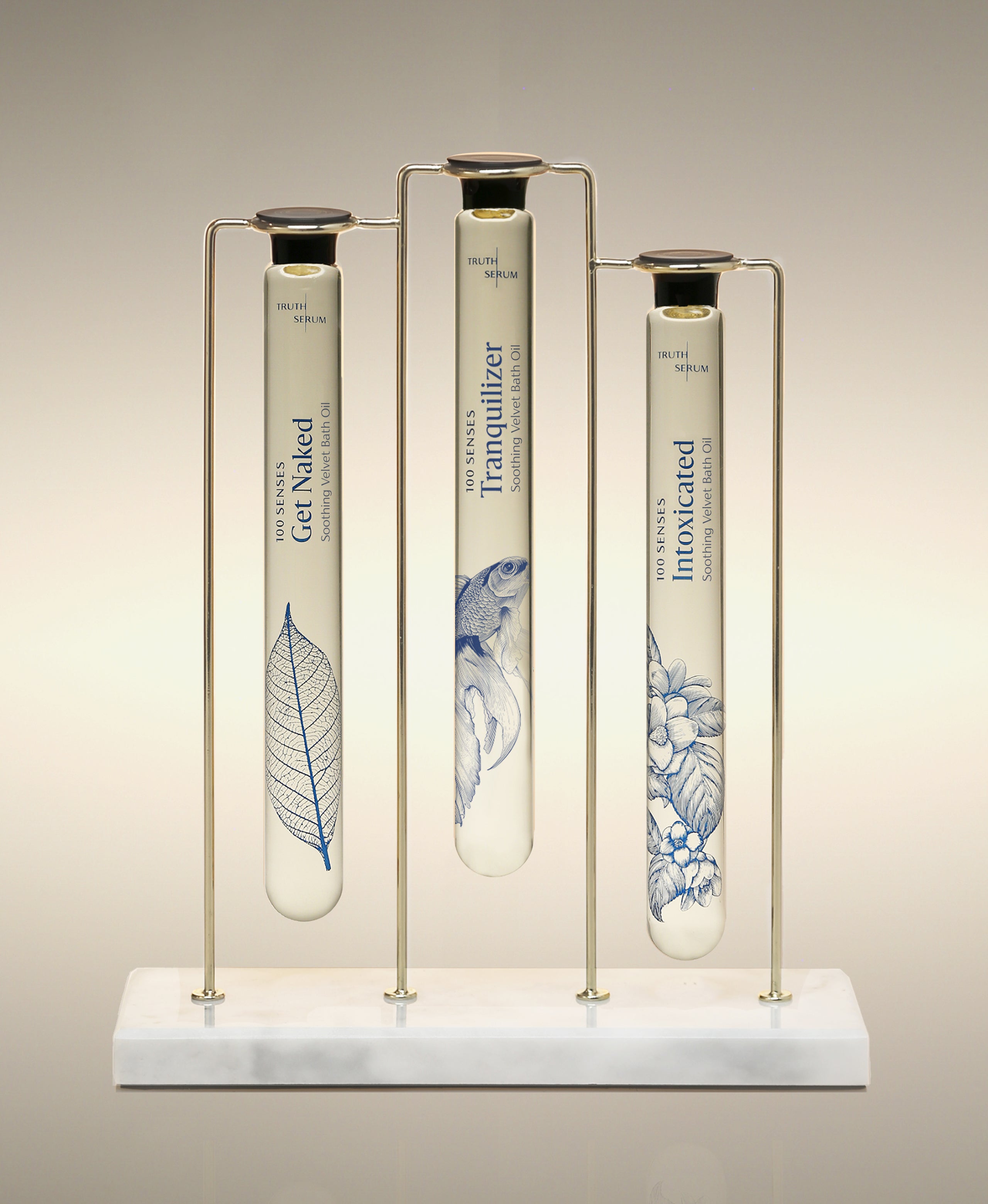 Get Naked, Tranquilizer and Intoxicated Velvet Bath Oils displayed in the Trio Cylinder Soak Stand in gold-and-marble.