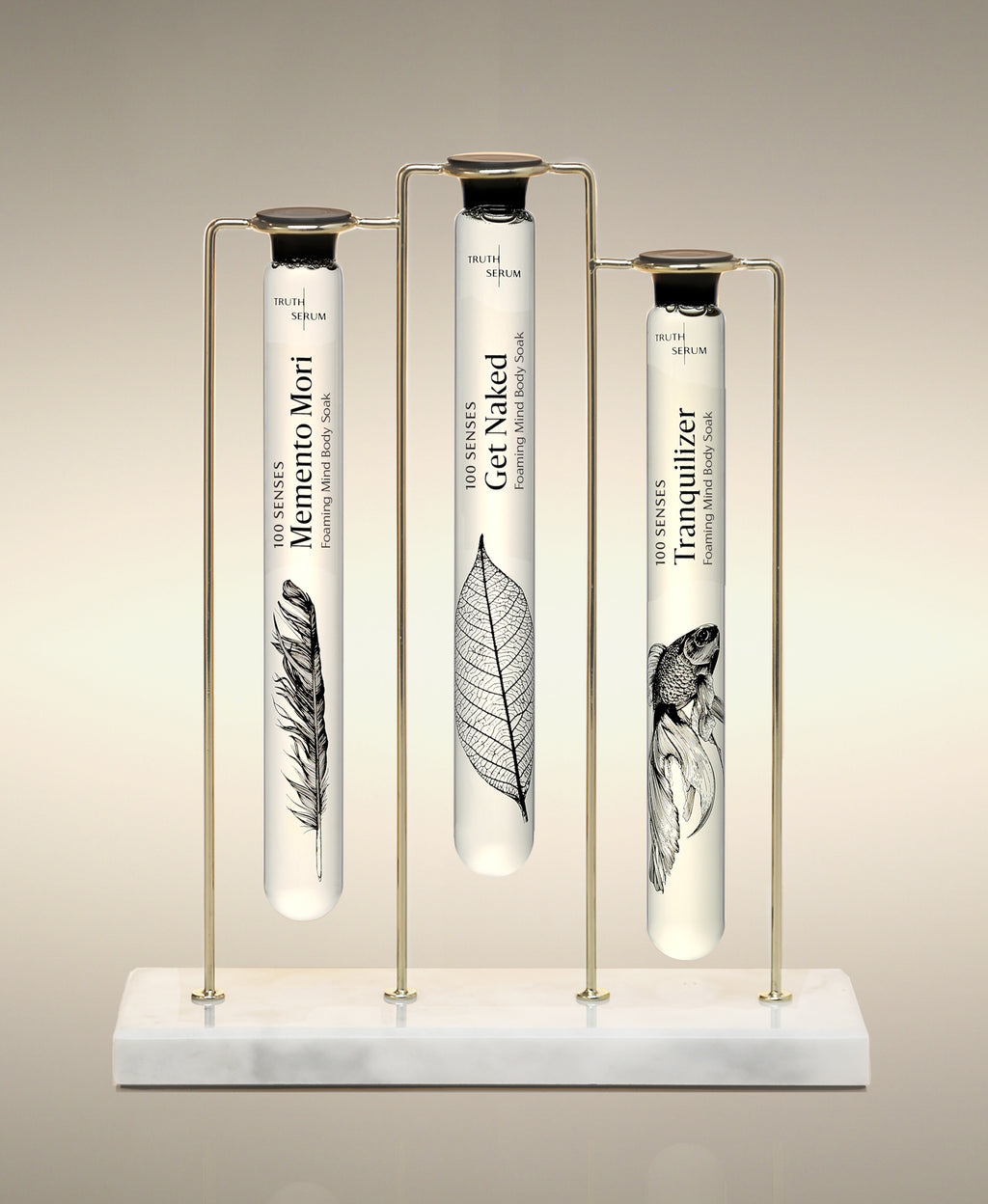 Memento Mori, Get Naked and Tranquilizer glass Foaming Cylinder Soaks displayed in the Trio Cylinder Soak Stand in gold-and-marble.