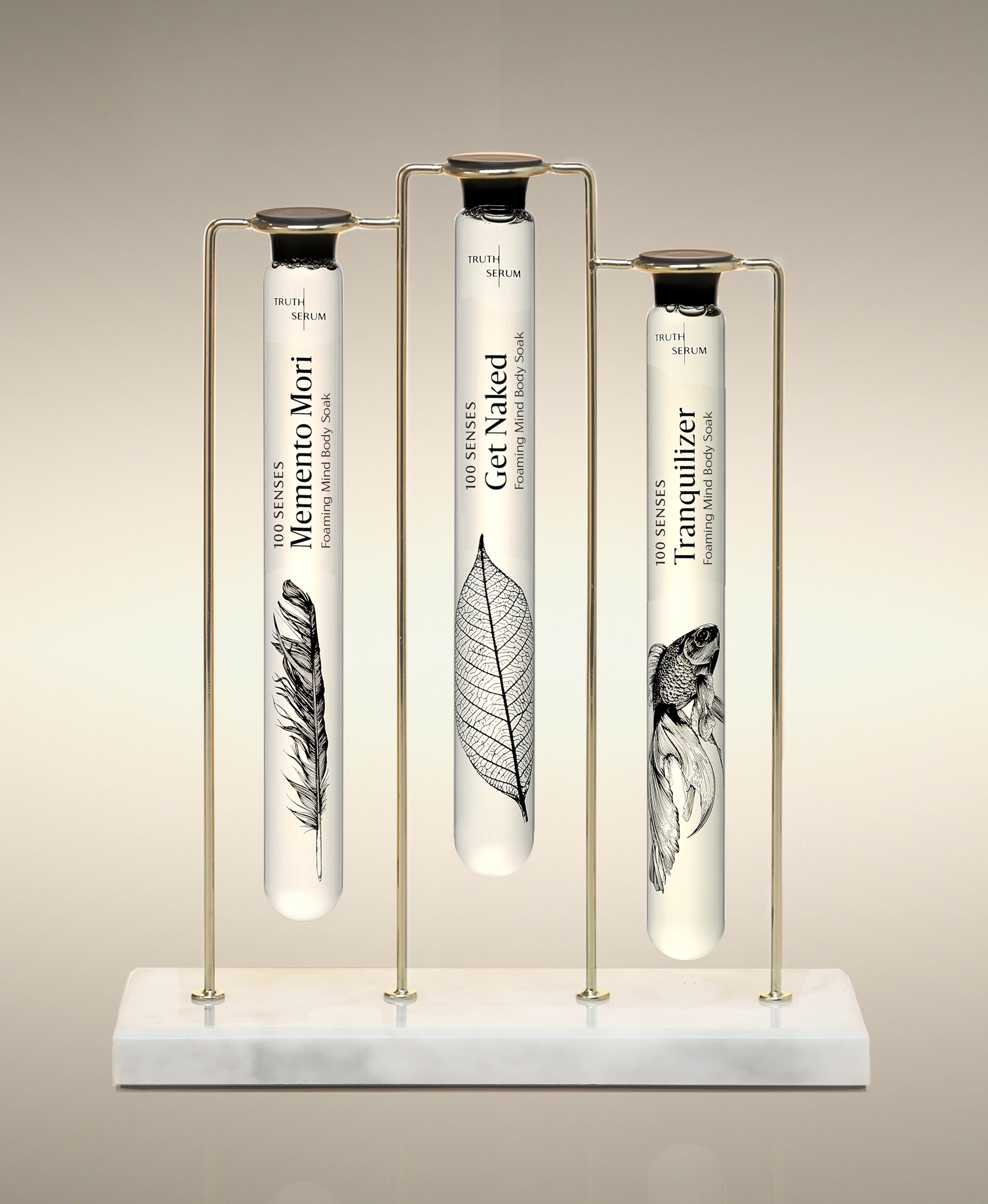 Memento Mori, Get Naked and Tranquilizer glass Foaming Cylinder Soaks displayed in the Trio Cylinder Soak Stand in gold-and-marble.