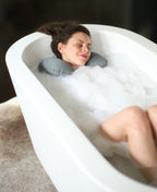 Person reclining in a foam-filled bath with a gray Head Floater snapped around their neck.