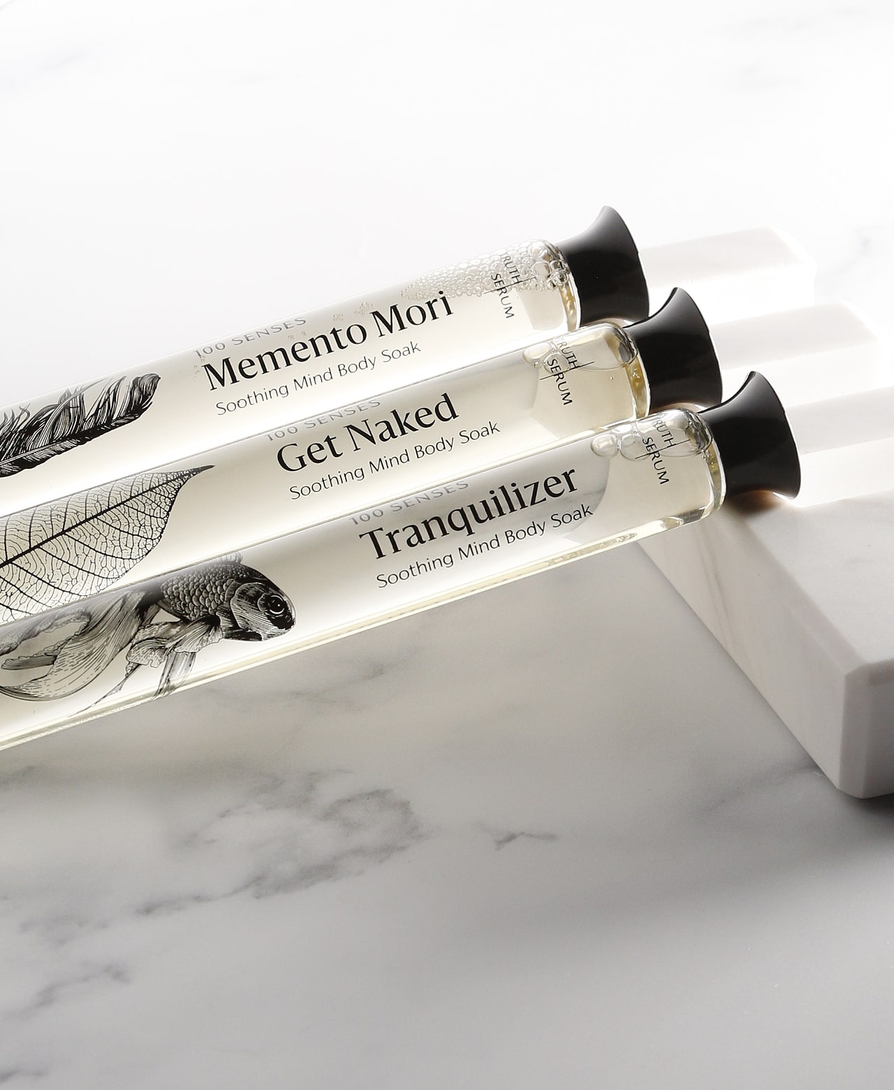 Memento Mori, Get Naked and Tranquilizer glass Foaming Cylinder Soaks resting on white marble.