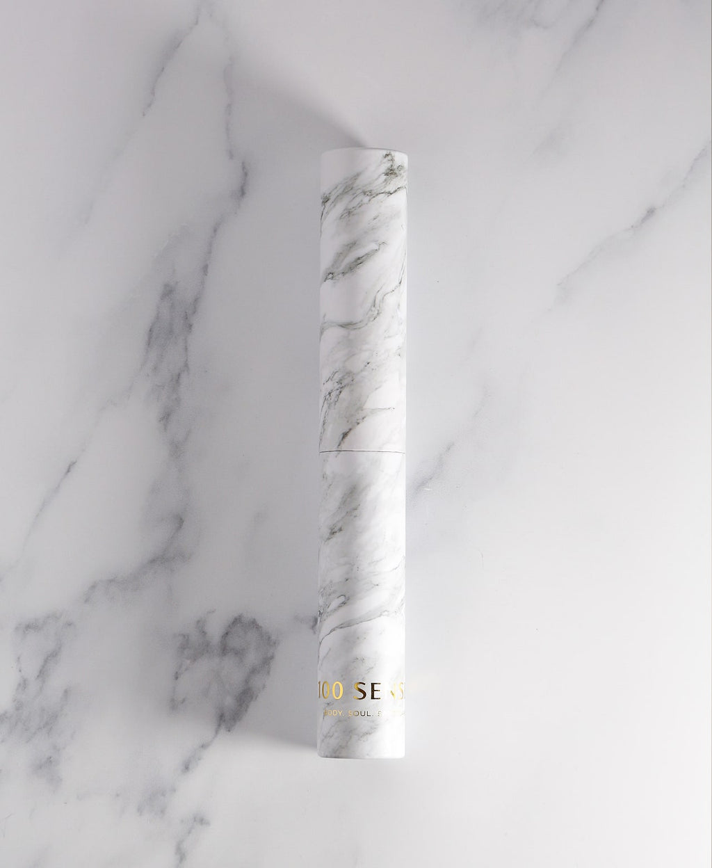 White marble-patterned glass Cylinder Soak Travel Case laying on a marble surface.