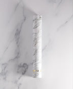 White marble-patterned glass Cylinder Soak Travel Case laying on a marble surface.