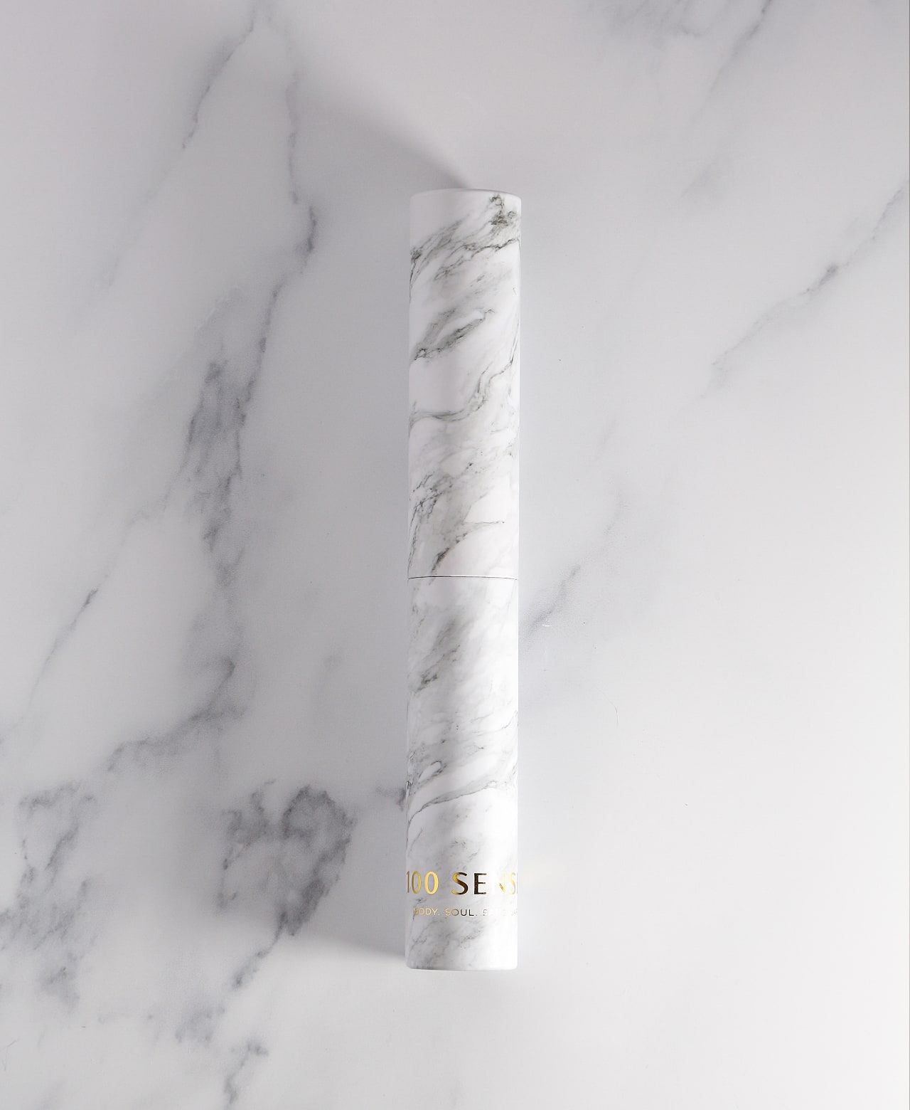 White marble-patterned glass Cylinder Soak Travel Case laying on a marble surface.