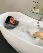 Person reclining in a bubble bath with a gray Head Floater snapped around their neck.