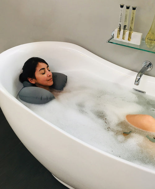 Person relaxing in a bubble bath with a gray Head Floater snapped around their neck.