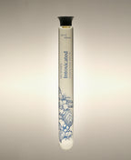 Intoxicated Cylinder Bath Oil glass bottle with a blue floral illustration, standing against a warm neutral background.