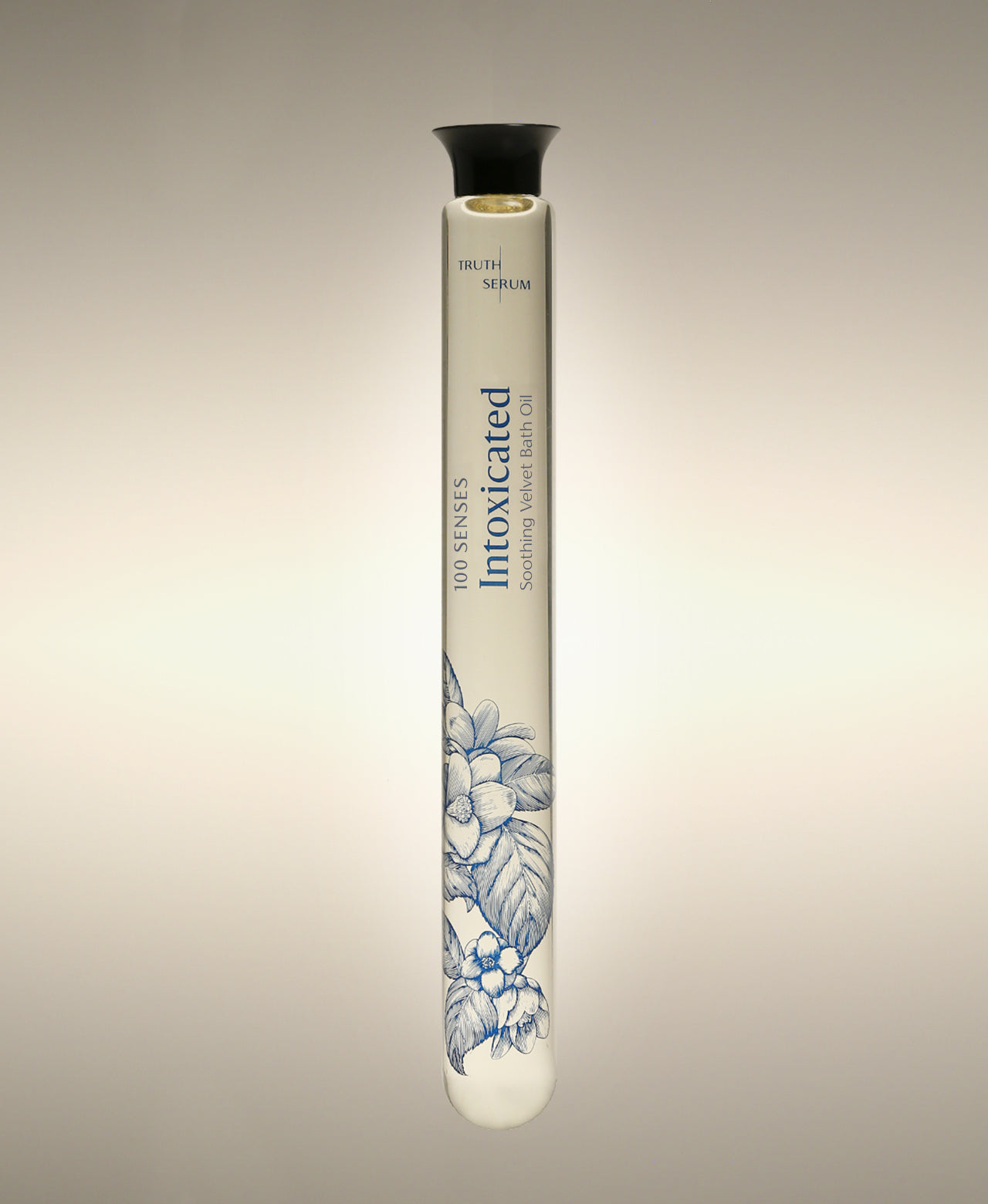 Intoxicated Cylinder Bath Oil glass bottle with a blue floral illustration, standing against a warm neutral background.