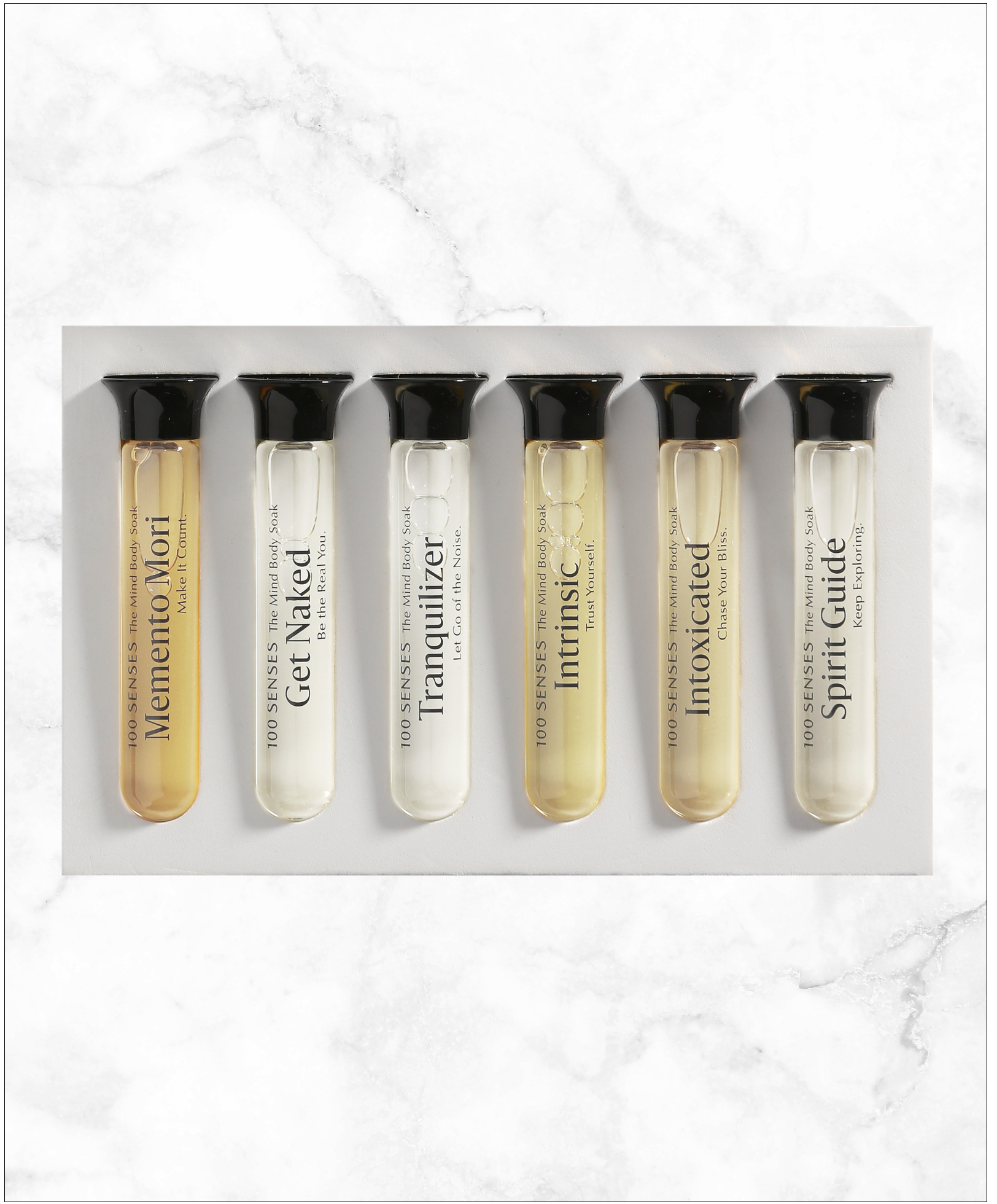 Six Mind/Body Soak Sampler glass vials arranged in their white tray on marble.