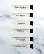 Six single-use glass vials of foaming bath soak arranged on white marble.