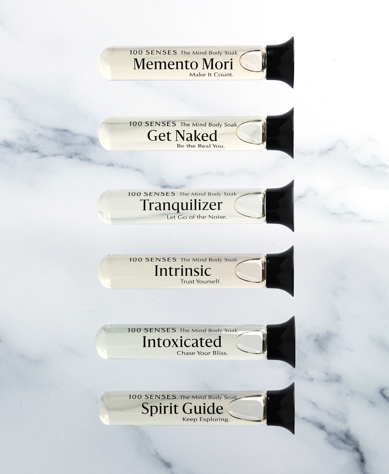 Six single-use glass vials of foaming bath soak arranged on white marble.